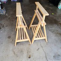 Two light wood adjustable sawhorses standing side by side on garage floor