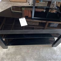 Front view of black glass TV stand showing three glass shelves