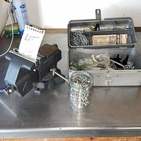 Bench vise left, toolbox open with hardware, mason jar front