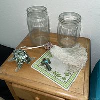 Group shot of glass turtle, cross on doily, beaded seashell item, two glass jars