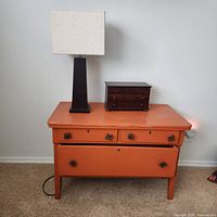 Front view of orange painted nightstand with drawers, lamp and jewelry box shown but not included