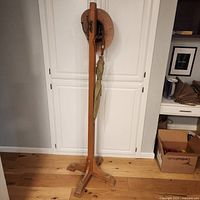 Full view of freestanding wooden hat rack with hat and umbrella for scale
