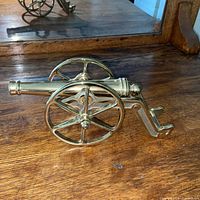 left side view showing entire brass cannon with spoked wheels and barrel