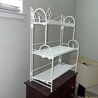 White metal rack standing on dresser, showing decorative scrolls and three levels