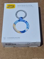 Front of sealed OtterBox Figura Series AirTag keyring holder box showing product image and included accessories note