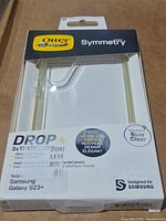 Front of retail box showing OtterBox Symmetry Series clear case for Samsung Galaxy S23+, visible yellowing on edges