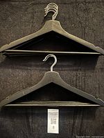 Front view showing stack of black wooden hangers with hooks