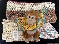 Stacked cream and multicolor blankets with plush monkey, small hat visible