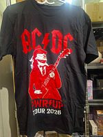 Front of black AC/DC PWR/UP Tour 2026 T-shirt hanging, shows Angus Young graphic