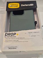 Front of open retail package showing olive OtterBox Defender case