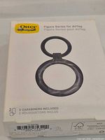 Front of retail box showing OtterBox Figura Series AirTag case and carabiner included note