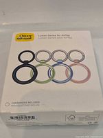 Front of retail box displaying four coloured OtterBox Lumen Series AirTag cases with carabiners