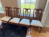 Four matching wooden side chairs with cream seats lined up against wall