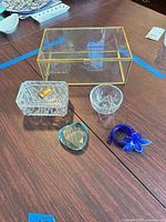 All items arranged on tabletop: glass box, ashtray with lighter, etched glass, teal heart, blue flower