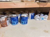 Multiple 1-gallon paint cans and sample pots on floor under shelf