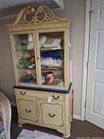 Full view of painted cabinet showing scrollwork crown, glass doors, drawer, and lower doors