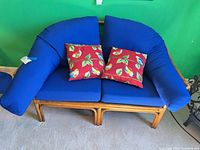 Front view of rattan loveseat with blue cushions and two red parrot pillows