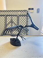Profile view of black cast iron bird sculpture showing skeletal design and curved base