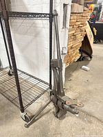 Full view of cast iron floor post vise leaning against wall and rack