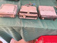 Three single-DIN car stereos lined up showing front panels and metal cases