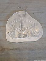 Front view of embossed metal plaque showing ship design and hanging string