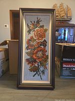 Full view of framed floral needlepoint tapestry standing upright