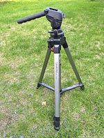 Tripod fully extended on grass showing pan-tilt head, handle, tripod legs