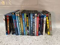 Row of 22 DVD cases standing on countertop, spines facing camera showing identifiable titles