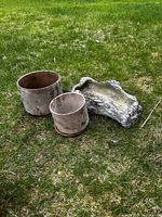 Two round ceramic pots and one ceramic log-style planter on grass