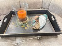 Tray, glass hurricane with candle, duck decoy displayed together on sofa
