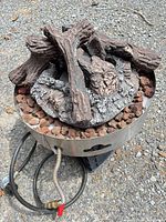 Top view of round stainless bowl filled with lava rock and ceramic logs, hose attached