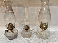 Front view of three glass hurricane lamps showing reservoirs, burners and chimneys
