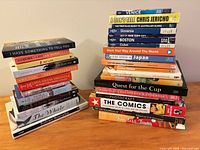 Stacks of approximately 30 books with visible titles across travel, memoir, cookery, sports and hobby subjects