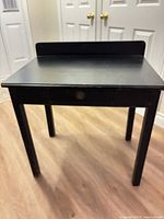 front angled view of black desk showing single drawer and raised back panel