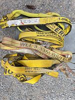 Pile of yellow ratchet straps with metal ratchets and hooks showing printed WLL ratings and brand names