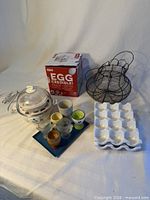 Group shot of egg cooker, box, ceramic tray, wire basket, egg cups
