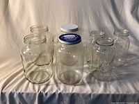 Six clear glass jars, two fitted with lids, displayed on cloth backdrop
