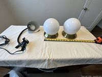 Full view of two Ikea globe fixtures and black clamp lamp on table with tape measure for scale