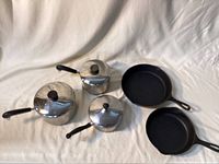 Top view of all cookware showing two cast iron pans and three stainless saucepans with lids
