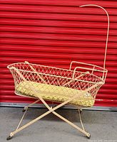 Full view of wrought iron doll cradle on X-frame with mattress and canopy rod