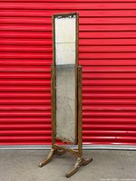 Full view of giltwood freestanding tilting mirror against red background