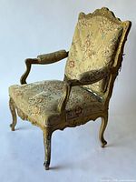 Full side perspective of one giltwood armchair showing frame and upholstery
