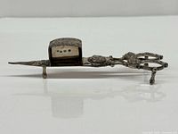 Side view of ornate silver wick trimming scissors with attached hallmarked snuffer box and tripod feet