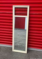 Full view of framed wall mirror leaning against red wall showing upper lattice panel and overall condition