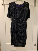 Full view of black dress with purple polka dots hanging on door