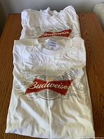 Two folded white Budweiser graphic T-shirts on table