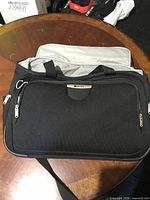 Front view of black Delsey soft-sided carry-on showing exterior pocket, handles and shoulder strap