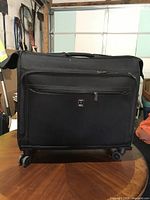 Front view of black Delsey wheeled garment suitcase showing exterior, spinner wheels and front pocket