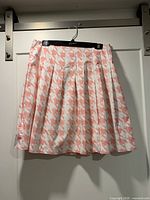 Front view of pleated pink and white houndstooth skirt on hanger