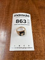 Ring on MaxSold tag, showing face, gold color, enamel, monogram